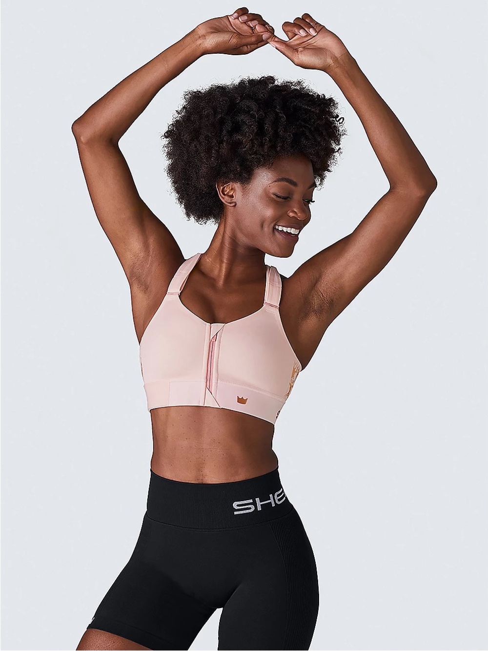 SHEFIT Women's Flex Medium-Impact Sports Bra in Blush with Gold Detailing.